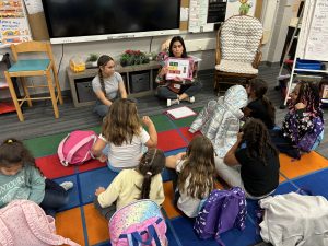 Adult reading book with children gathered around listening.